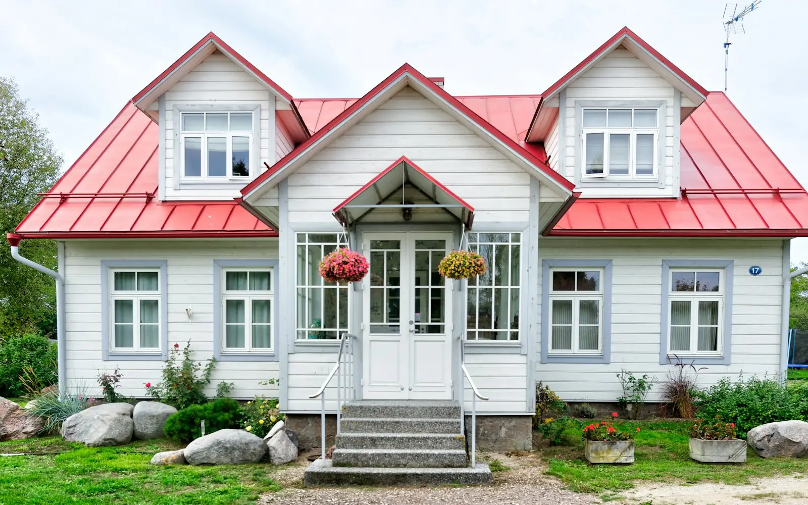 White cottage with red roof and colorful flower beds in front