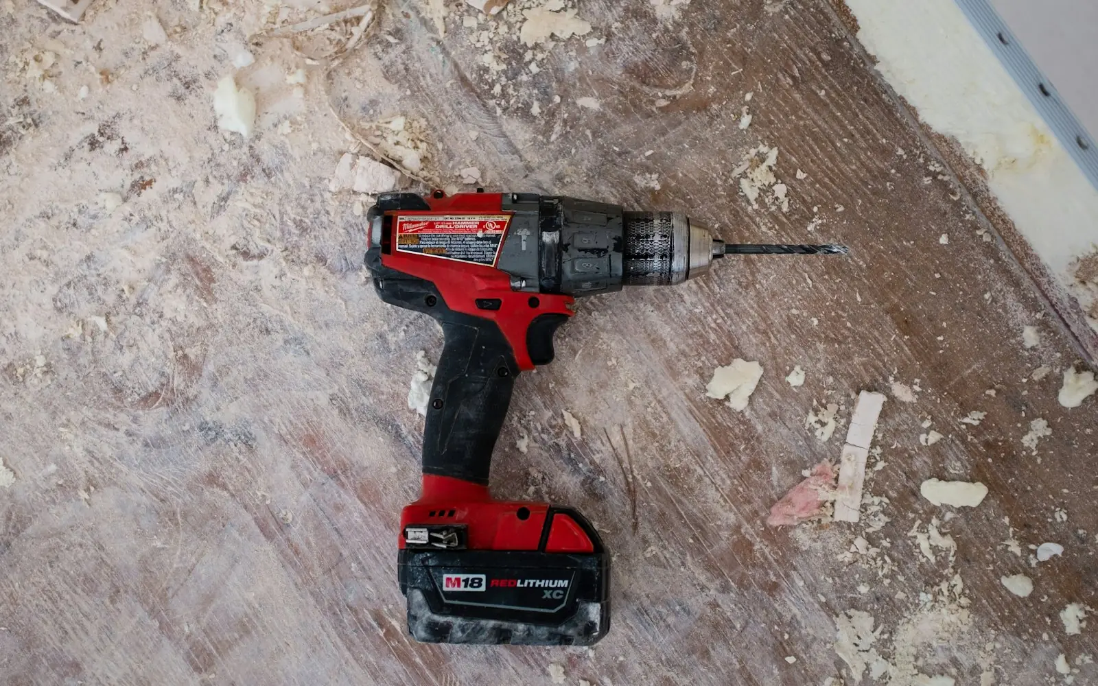 Red cordless drill resting on a dusty wooden workbench