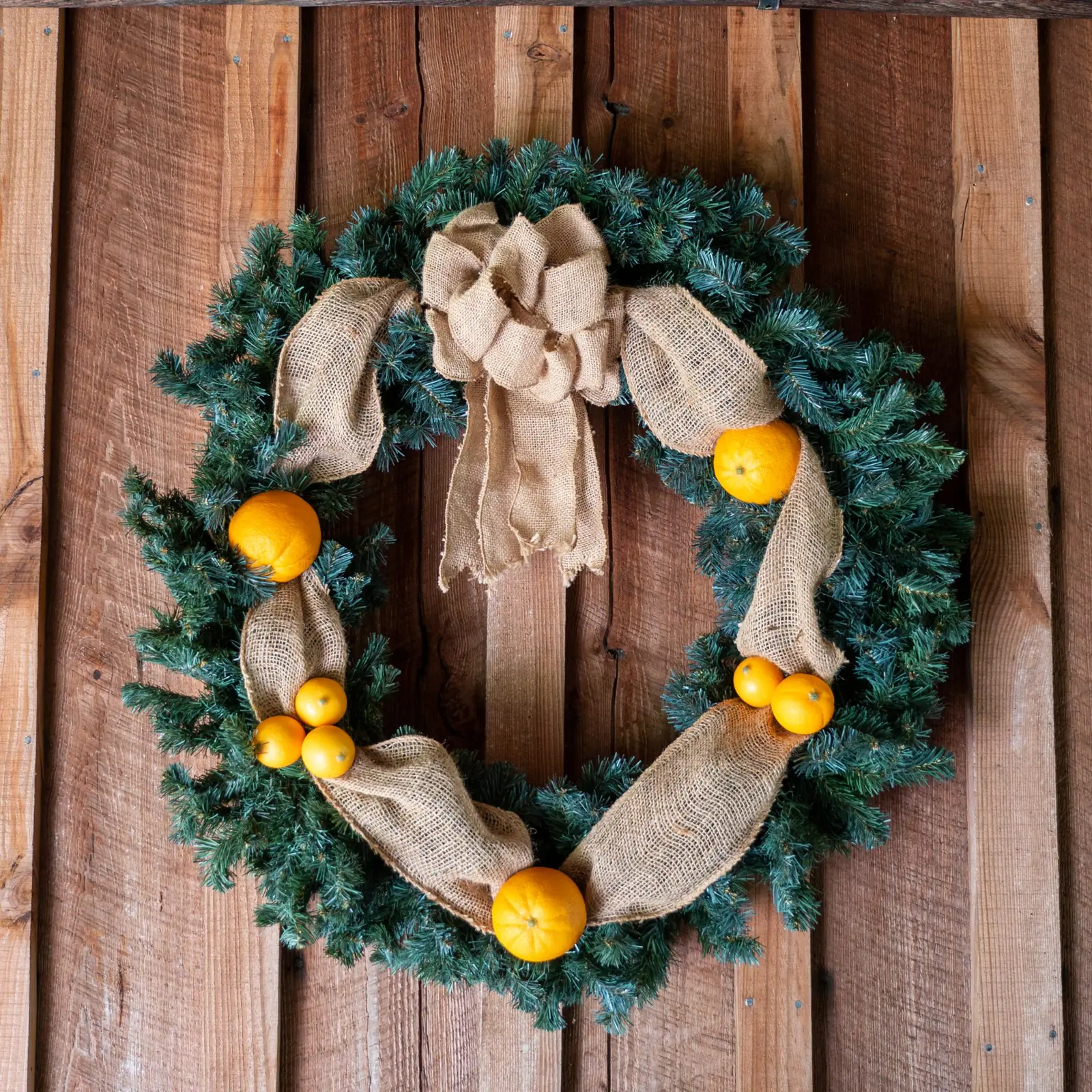 Evergreen wreath with a burlap bow hanging on a rustic wood door