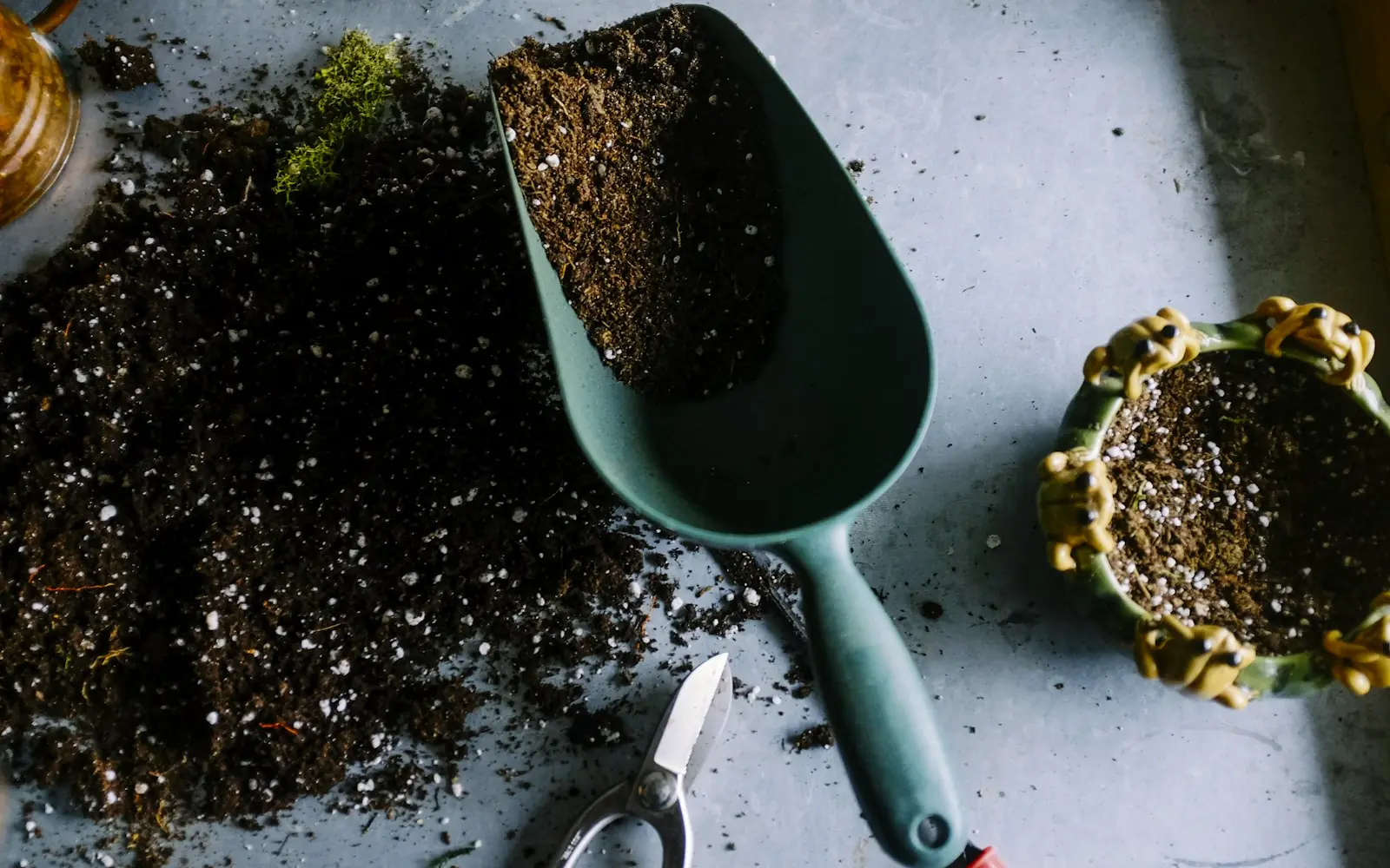 Garden trowel scooping rich dark soil next to potted plants