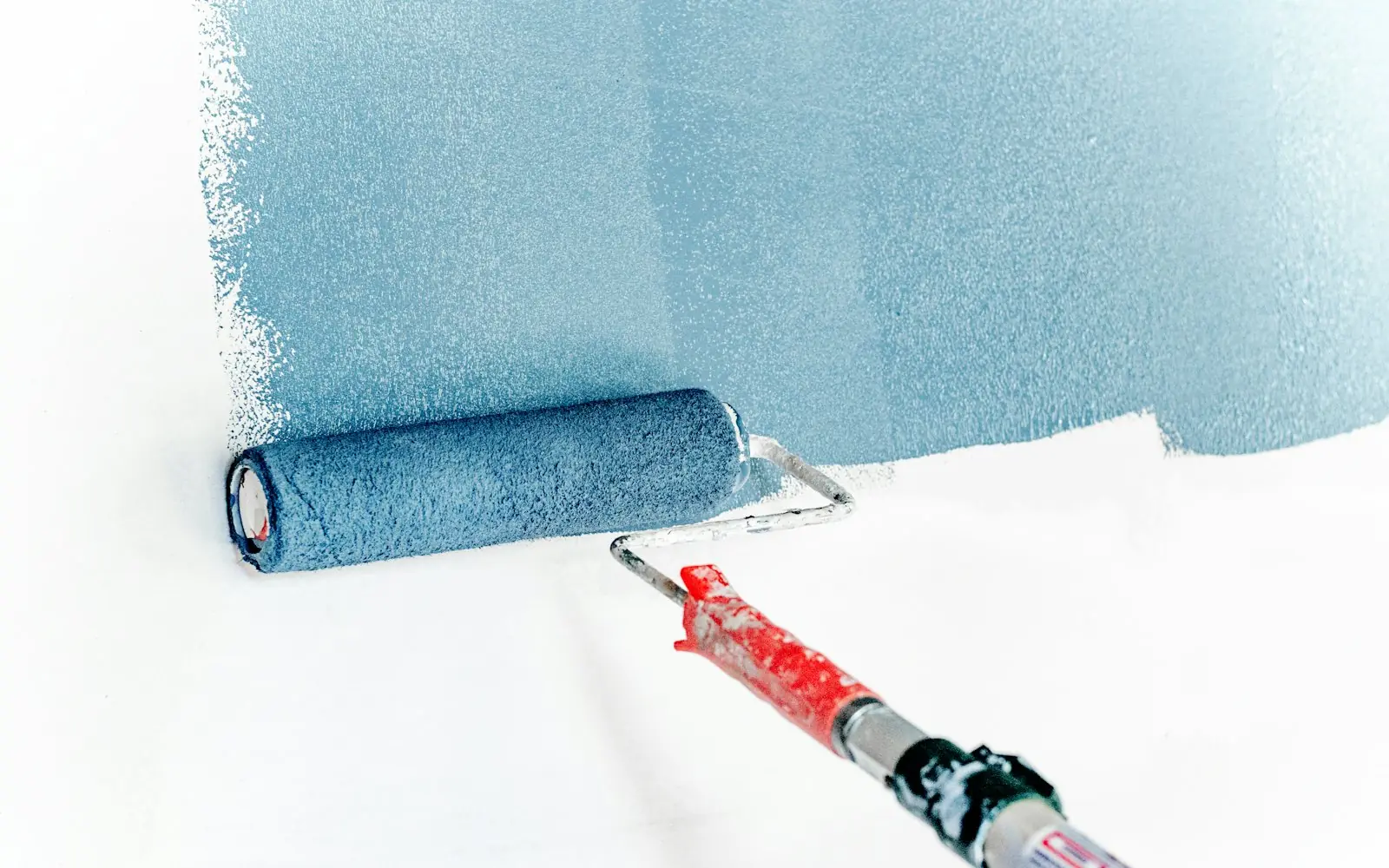 Paint roller rolling fresh pale blue paint onto a white wall